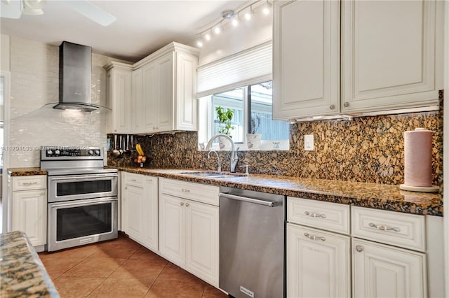 kitchen with light tile patterned floors, appliances with stainless steel finishes, wall chimney range hood, backsplash, and a sink