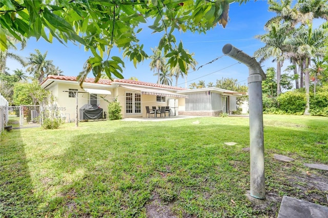 rear view of property with fence, a patio, a tiled roof, a lawn, and french doors