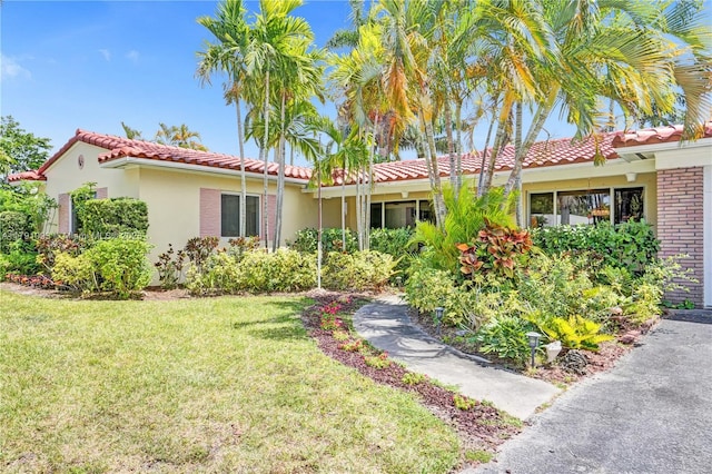ranch-style house with brick siding, stucco siding, a tile roof, and a front yard