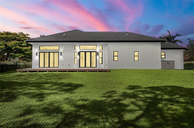 499 SW Squire Johns Ln, Palm City, FL 34990 - back of house at dusk with a lawn, a deck, and stucco siding