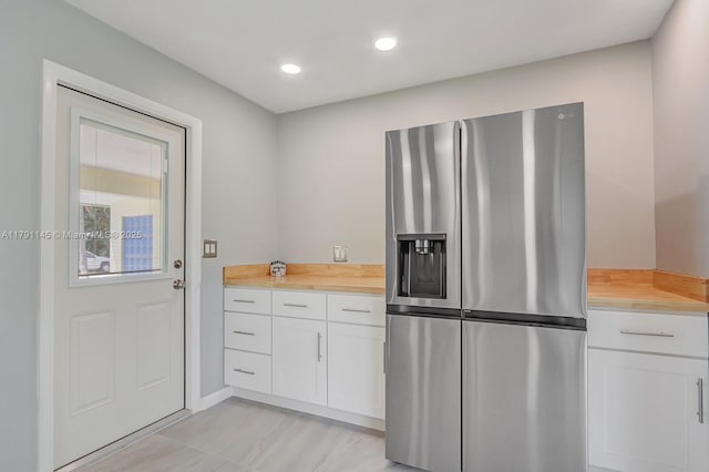 kitchen featuring stainless steel fridge, wood counters, white cabinetry, recessed lighting, and baseboards
