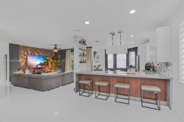 kitchen with a peninsula, a kitchen bar, stainless steel fridge, light countertops, and white cabinetry