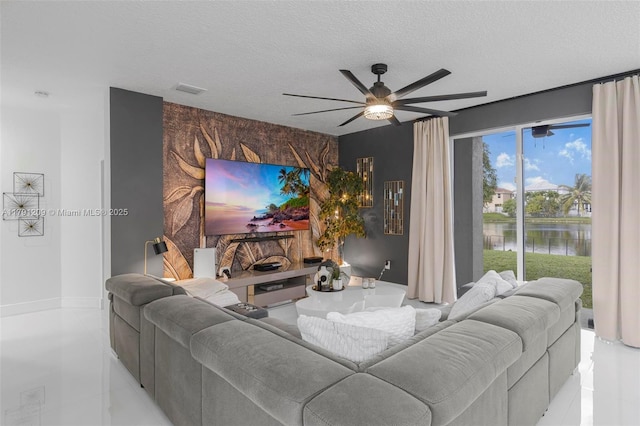 tiled living room featuring a ceiling fan, a textured ceiling, visible vents, baseboards, and an accent wall