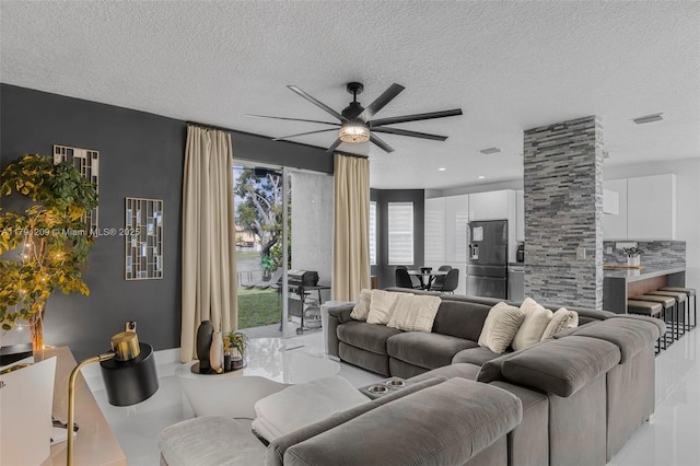 living area with a ceiling fan, a textured ceiling, and visible vents