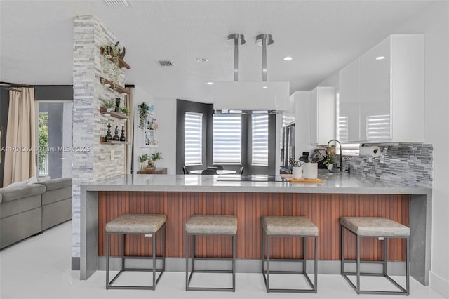 kitchen with freestanding refrigerator, a peninsula, light countertops, white cabinetry, and tasteful backsplash