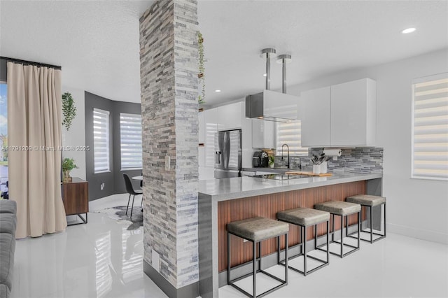 kitchen with light tile patterned flooring, a breakfast bar, stainless steel fridge, white cabinetry, and tasteful backsplash