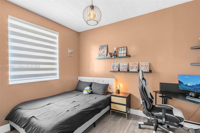 bedroom featuring baseboards, a textured ceiling, and wood finished floors