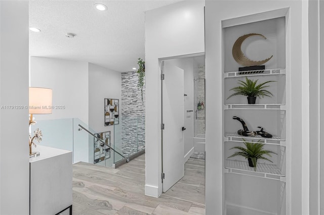 hall with recessed lighting, a textured ceiling, wood finished floors, and an upstairs landing