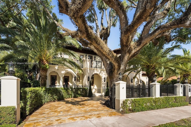 mediterranean / spanish house with a fenced front yard, stucco siding, a gate, and a balcony