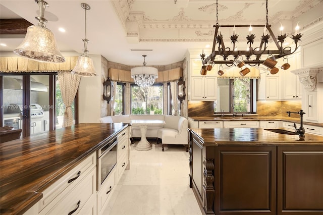 kitchen with built in microwave, wood counters, a chandelier, a healthy amount of sunlight, and dark brown cabinets