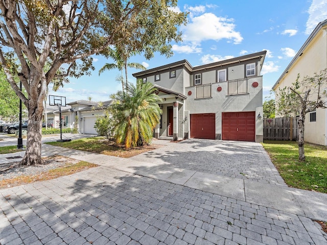 view of front facade featuring fence, a balcony, decorative driveway, stucco siding, and an attached garage