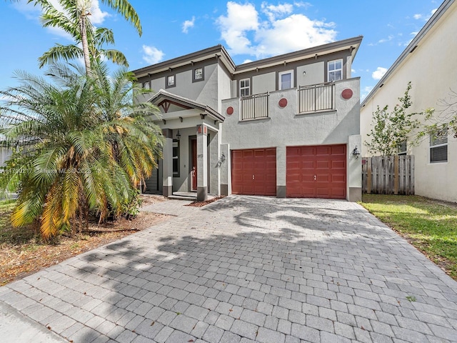 view of front of house featuring fence, a balcony, decorative driveway, stucco siding, and an attached garage