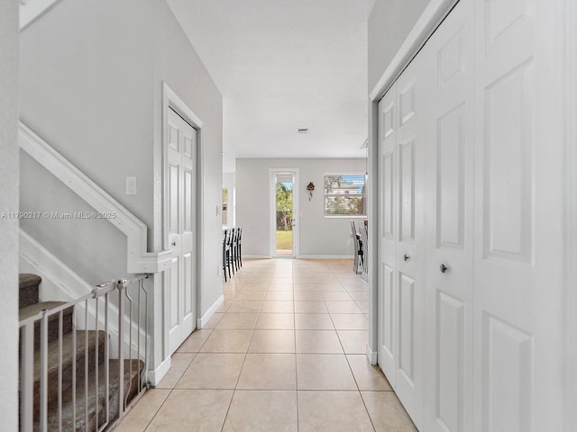hall with light tile patterned floors, baseboards, and stairway