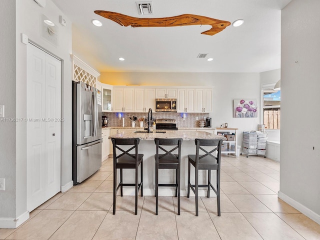 kitchen featuring appliances with stainless steel finishes, a sink, a breakfast bar area, decorative backsplash, and visible vents