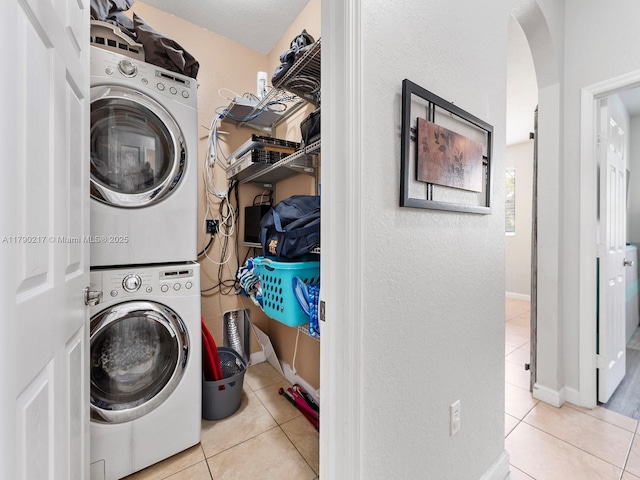 washroom with arched walkways, tile patterned flooring, laundry area, and stacked washer and dryer