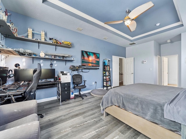 bedroom with ceiling fan, visible vents, wood finished floors, baseboards, and a tray ceiling