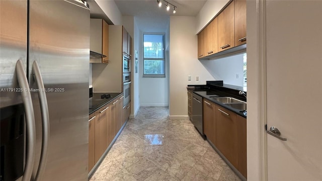 kitchen with a sink, dark countertops, stainless steel appliances, baseboards, and under cabinet range hood