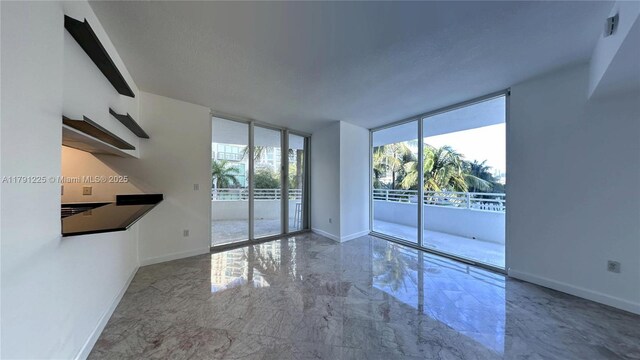 spare room featuring marble finish floor, expansive windows, and baseboards
