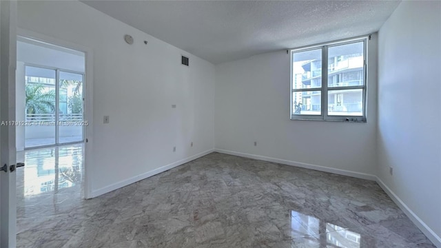 empty room featuring a textured ceiling, visible vents, marble finish floor, and baseboards