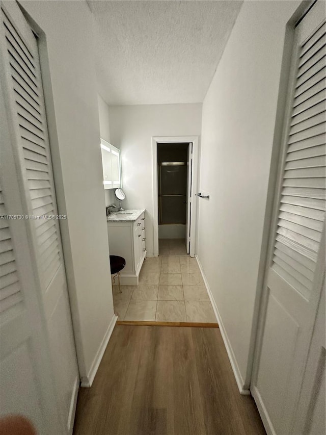 300 Bayview Dr Unit 315, Sunny Isles Beach, FL 33160 - hall featuring baseboards, a sink, light wood-style flooring, and a textured ceiling