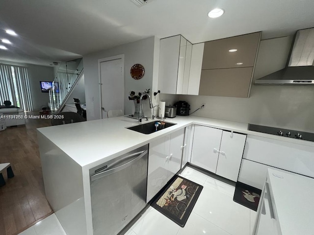 kitchen featuring wall chimney range hood, black electric cooktop, dishwasher, a sink, and a peninsula