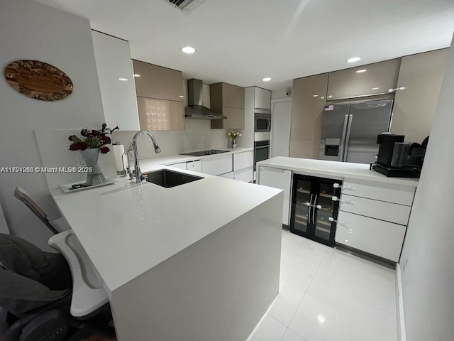 kitchen with a peninsula, stainless steel appliances, a sink, wall chimney exhaust hood, and modern cabinets