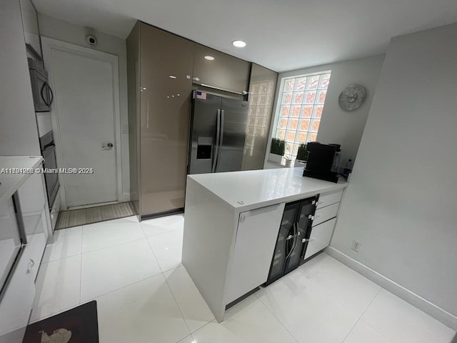 kitchen featuring light countertops, baseboards, light tile patterned flooring, a peninsula, and stainless steel fridge