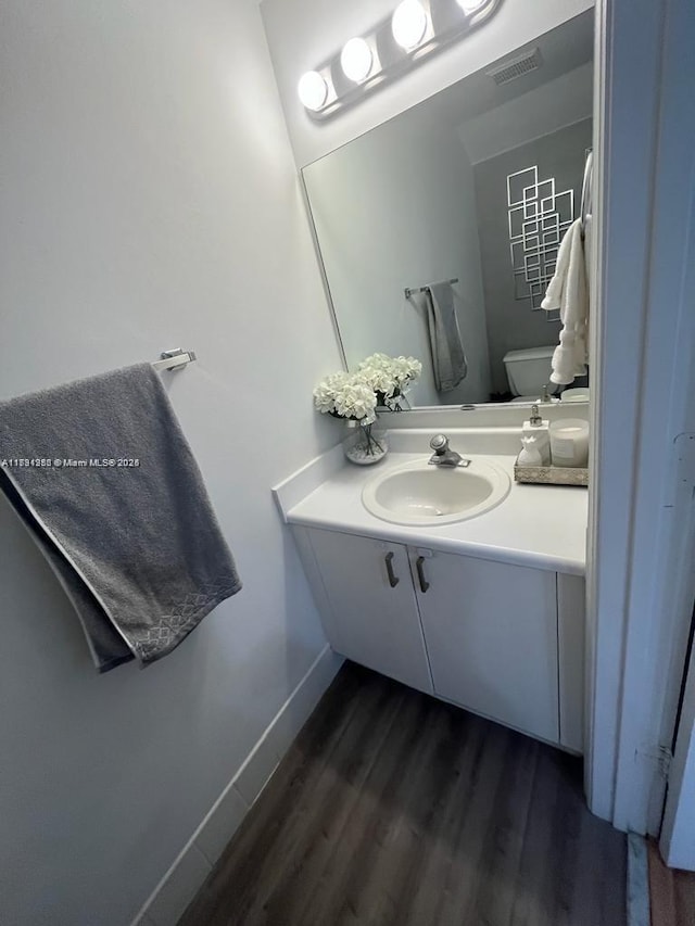 bathroom featuring vanity, toilet, visible vents, baseboards, and wood finished floors