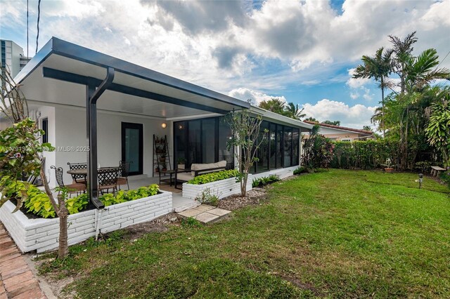 rear view of house featuring a patio, a yard, stucco siding, and a sunroom