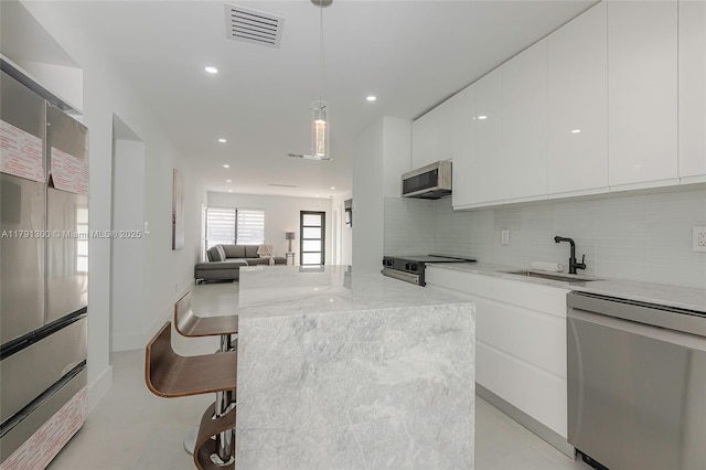 kitchen with appliances with stainless steel finishes, white cabinets, a sink, visible vents, and modern cabinets