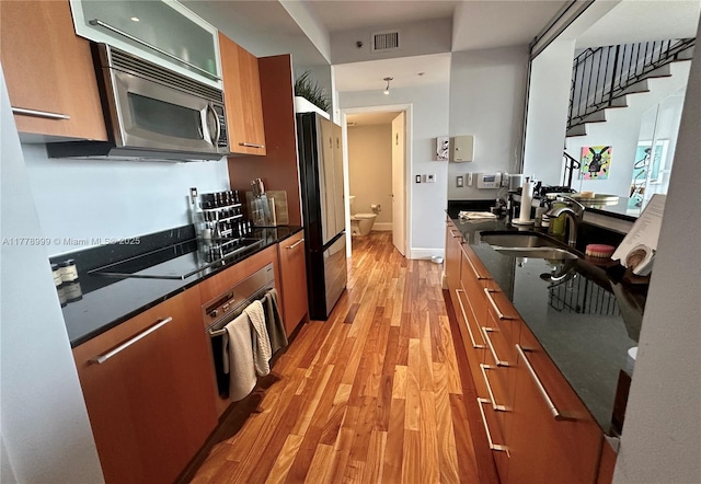 kitchen with a sink, stainless steel appliances, brown cabinetry, visible vents, and light wood-style flooring