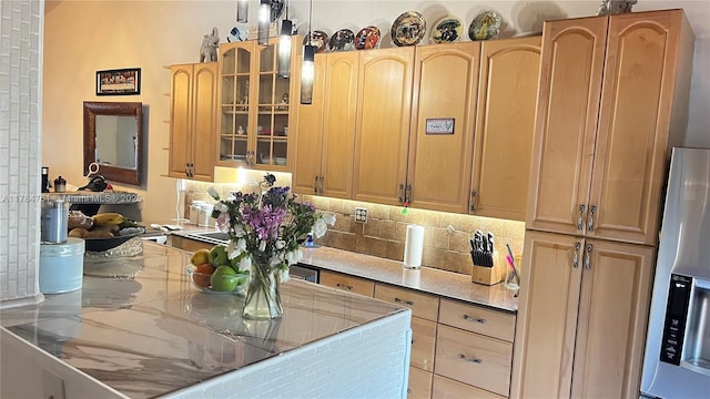 kitchen with stainless steel refrigerator with ice dispenser, tasteful backsplash, light countertops, glass insert cabinets, and light brown cabinets