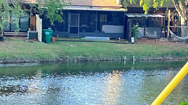 rear view of property featuring central air condition unit, a water view, a yard, and a sunroom