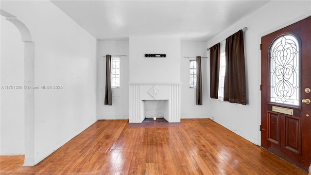 foyer featuring wood-type flooring, arched walkways, and a premium fireplace