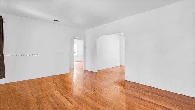 unfurnished room with visible vents, arched walkways, and light wood-style flooring