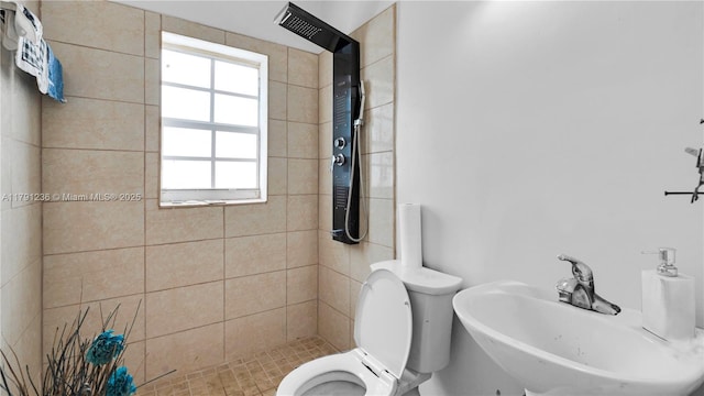 bathroom with a tile shower, toilet, and a sink