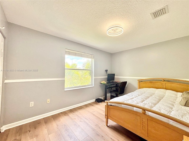 bedroom featuring light wood-style floors, a textured ceiling, baseboards, and visible vents