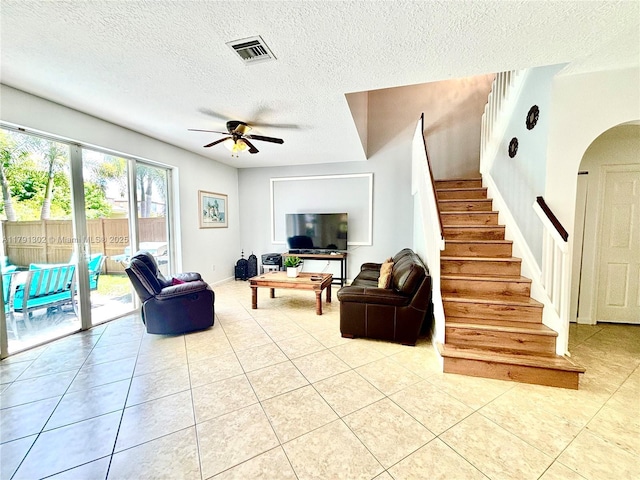 living area with ceiling fan, a textured ceiling, arched walkways, light tile patterned floors, and stairway