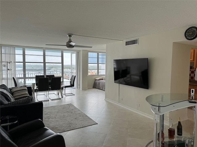 living area featuring baseboards, visible vents, a ceiling fan, a textured ceiling, and light tile patterned flooring