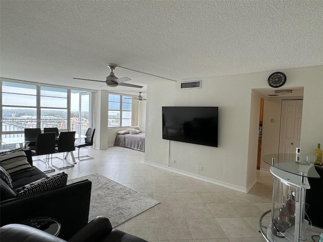 living area featuring light tile patterned flooring, visible vents, ceiling fan, and a textured ceiling