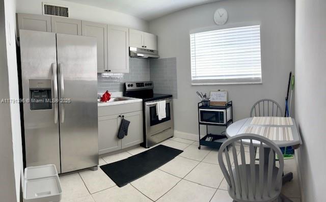 kitchen featuring light tile patterned floors, under cabinet range hood, appliances with stainless steel finishes, backsplash, and visible vents