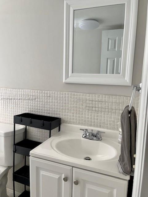 half bathroom featuring backsplash, toilet, and vanity