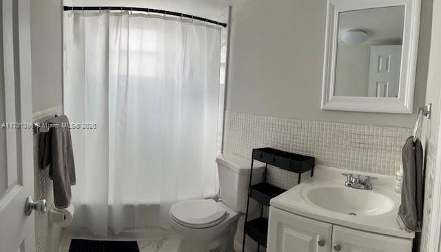 full bath featuring wainscoting, tile walls, shower / bath combo with shower curtain, toilet, and vanity