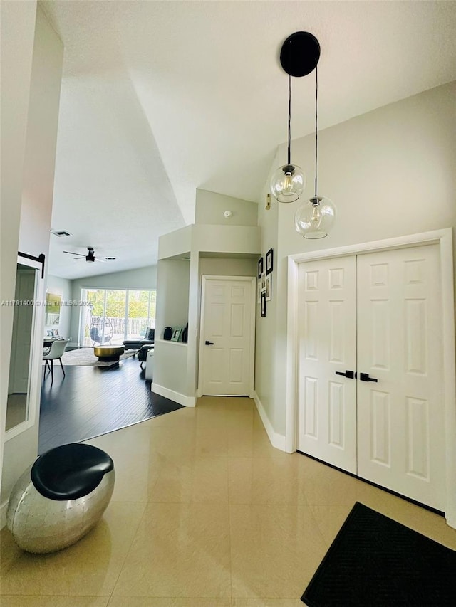 tiled foyer entrance featuring lofted ceiling, a barn door, a ceiling fan, and baseboards