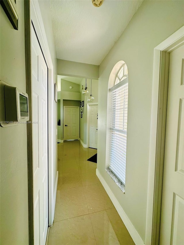 corridor featuring light tile patterned floors, a textured ceiling, and baseboards