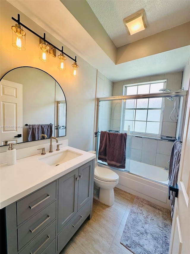 full bathroom featuring a textured ceiling, combined bath / shower with glass door, toilet, tile patterned floors, and vanity