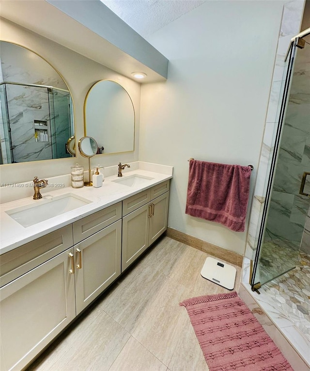 full bath with a marble finish shower, a textured ceiling, double vanity, and a sink