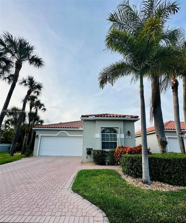 mediterranean / spanish-style home featuring stucco siding, decorative driveway, a tiled roof, and a garage