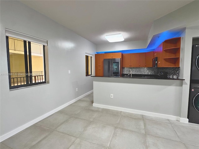 kitchen featuring smart refrigerator, stacked washer and clothes dryer, backsplash, a peninsula, and dark countertops
