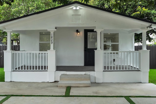 view of front of home with stucco siding, covered porch, and fence